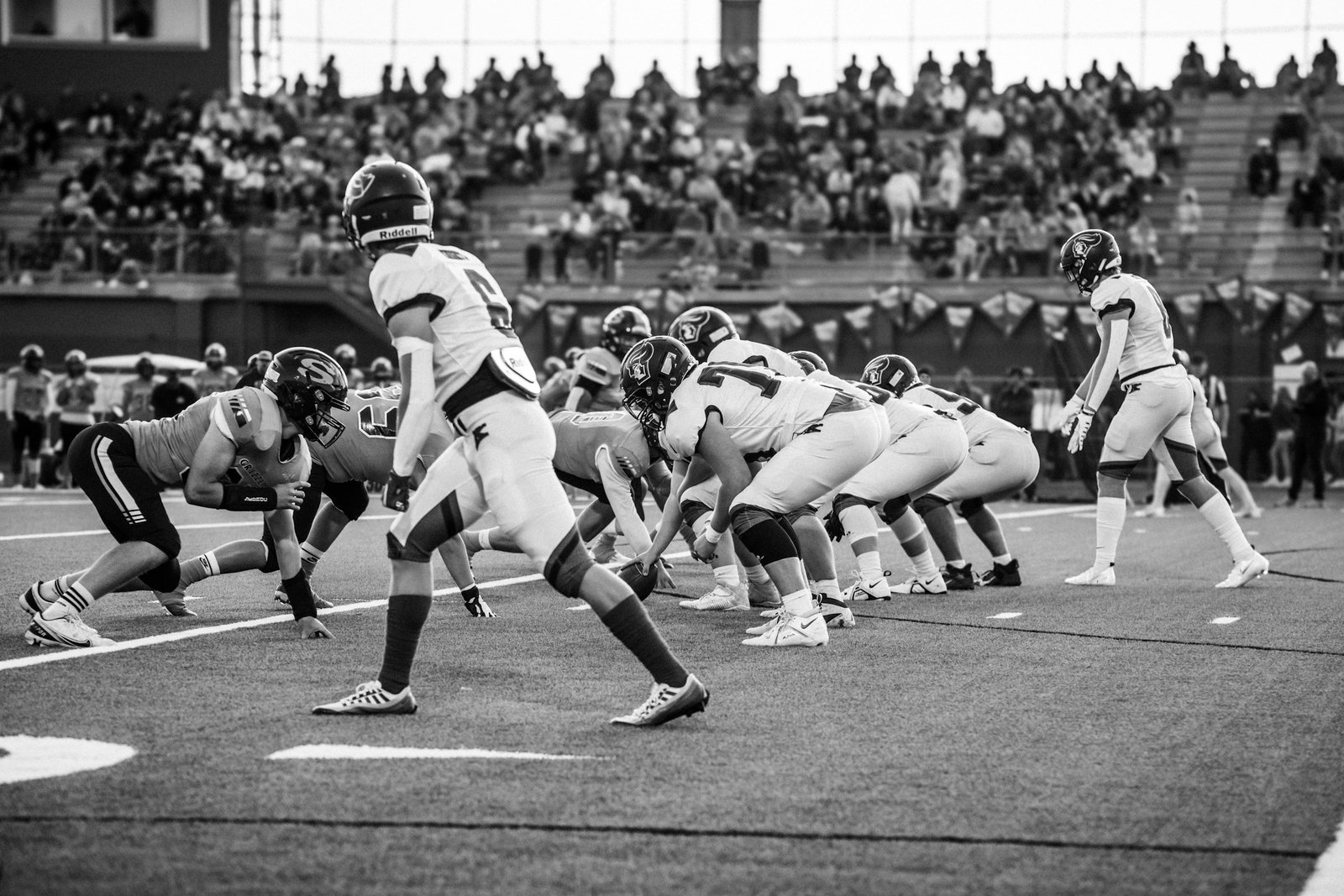 American football players in helmets and uniforms huddle on a marked gridiron