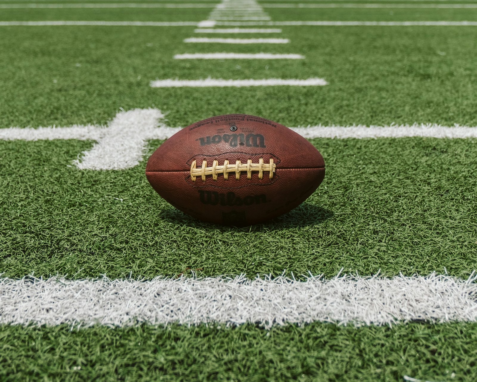 Brown Wilson American football resting on artificial turf and white yard lines