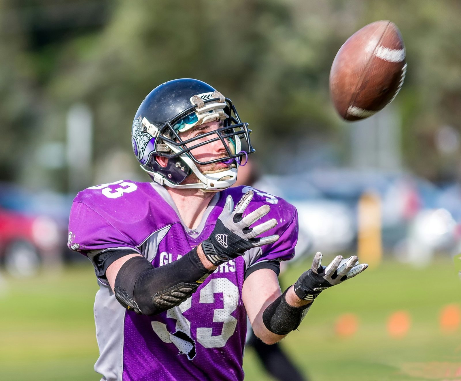 American football player reaching to catch an oval ball on the field